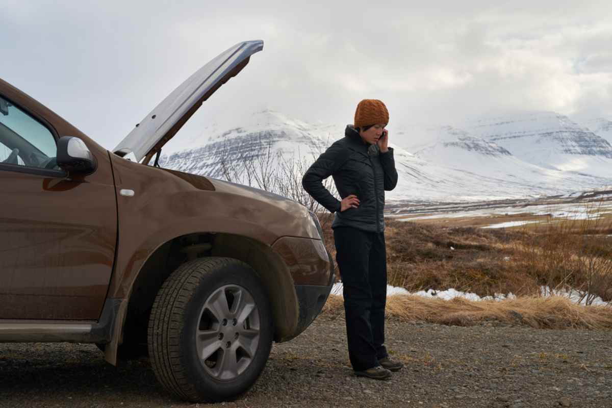 Driver calling for roadside assistance beside a car with the hood up in snowy Iceland.