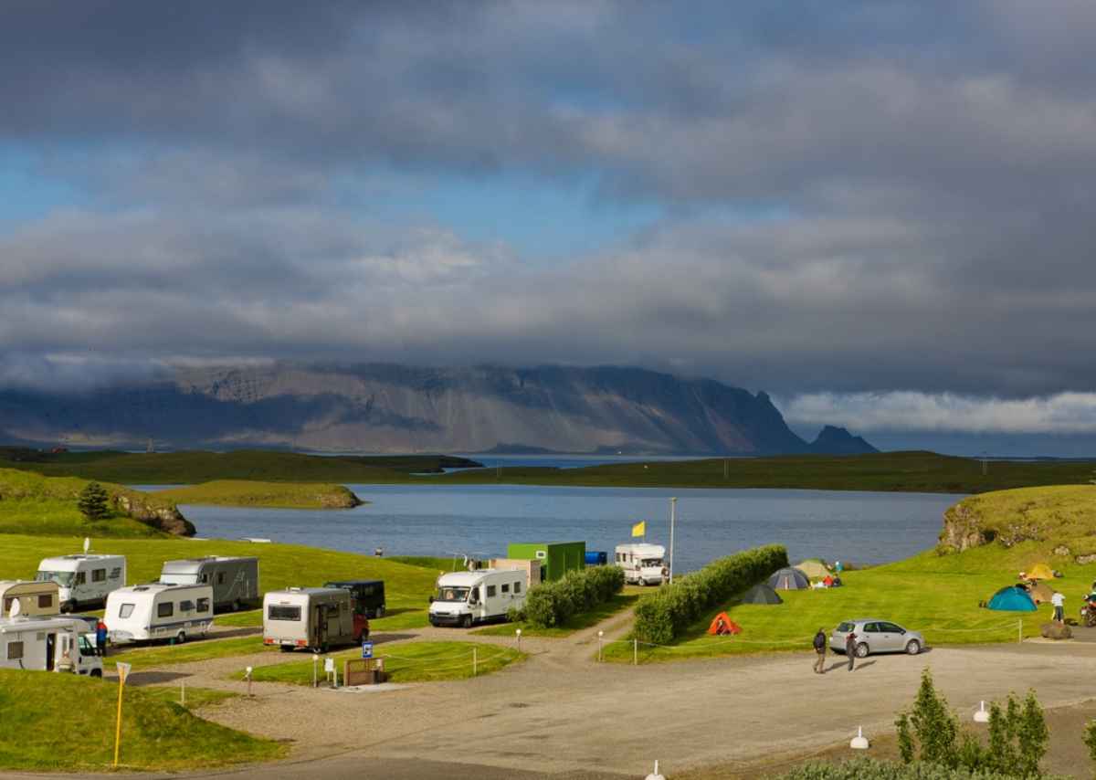 A group of white campers and motorhomes parked near a body of water in Iceland.