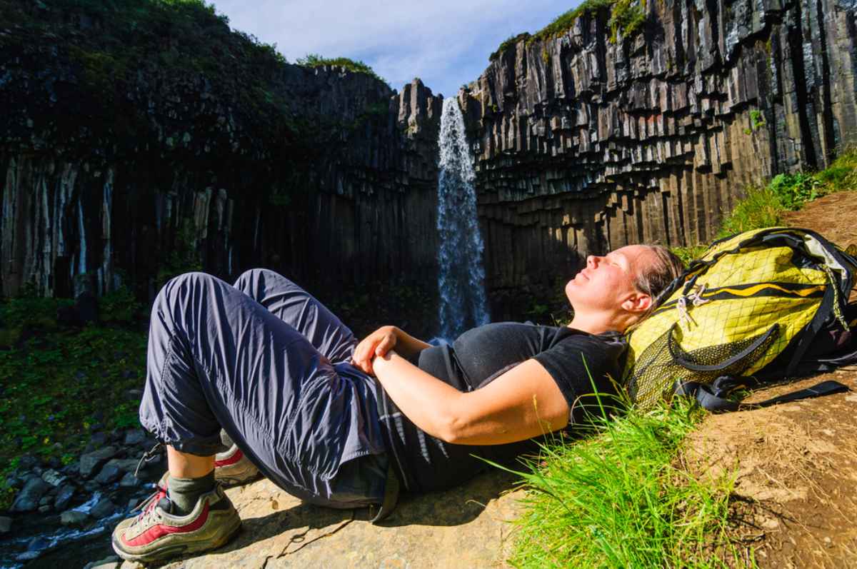 Traveler resting on soft Icelandic moss by a waterfall.