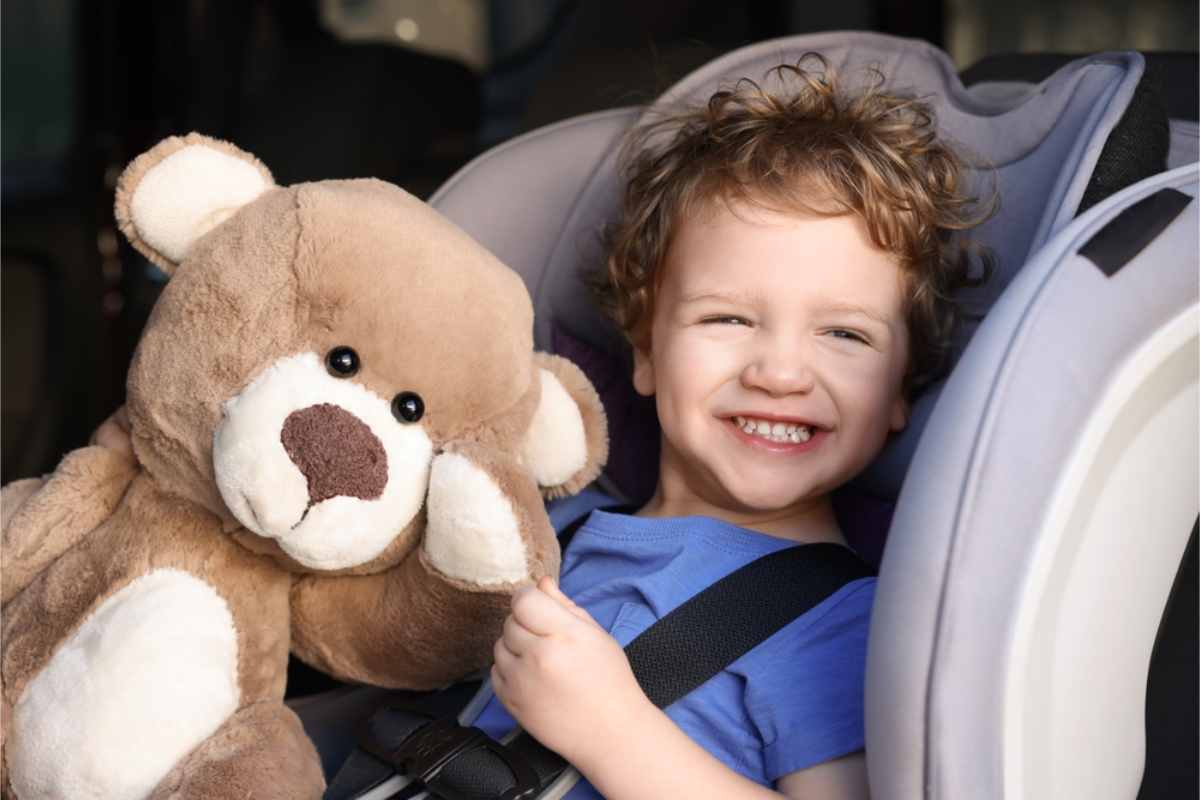 Kid holding his teddy bear while sitting on a child seat 