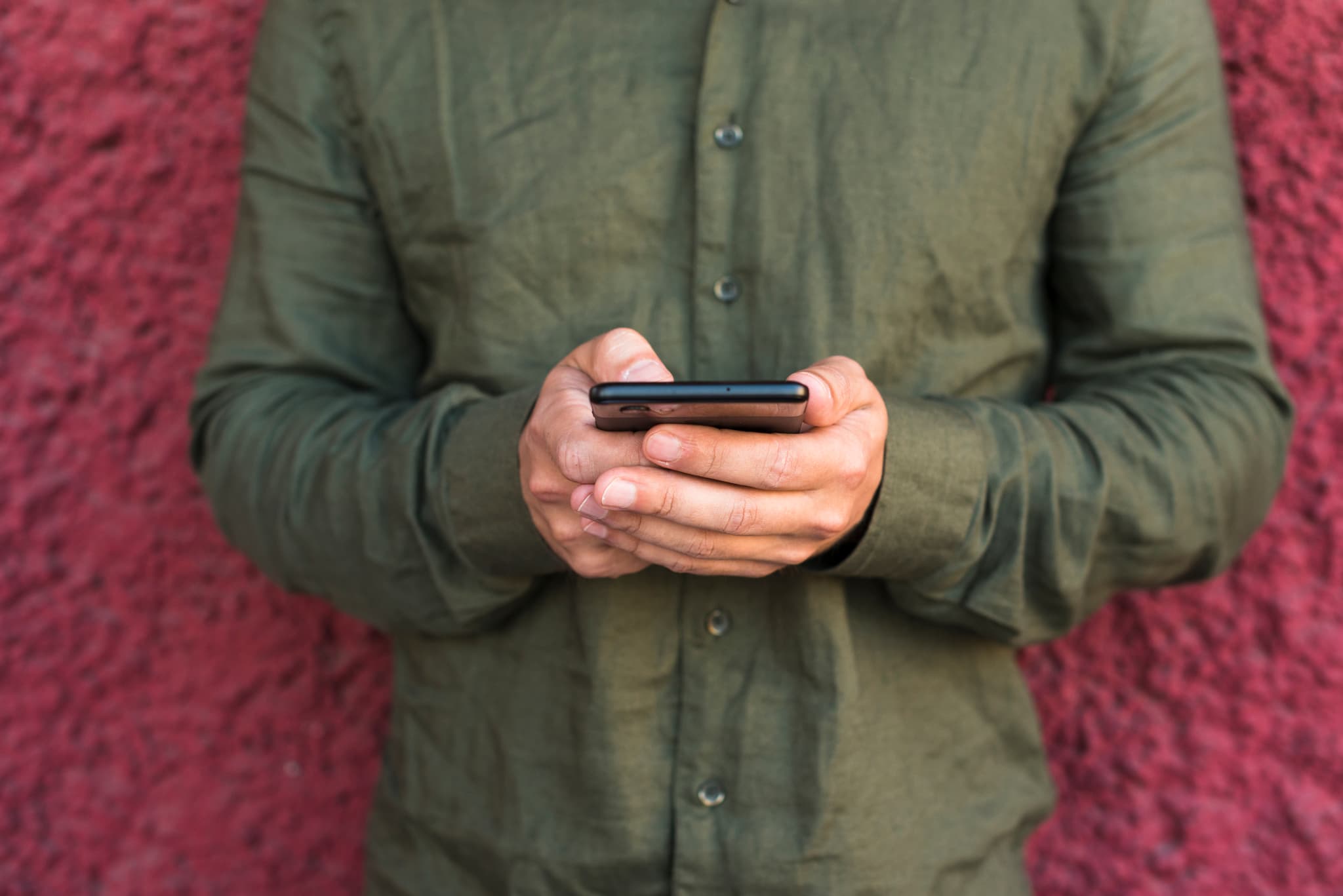Close-up of a person in a green shirt using a smartphone against a red wall, illustrating easy 48-hour cancellation for Iceland campervan rentals.