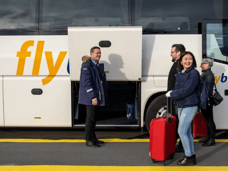 Smiling travelers with red suitcases boarding an airport shuttle at Keflavik, illustrating free pickup and drop-off for Iceland campervan rentals.