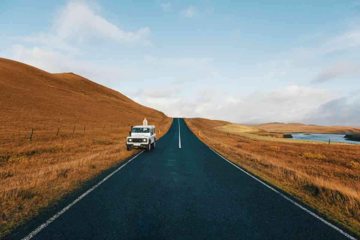Empty asphalt road through rolling brown valleys with a river and a parked Defender.