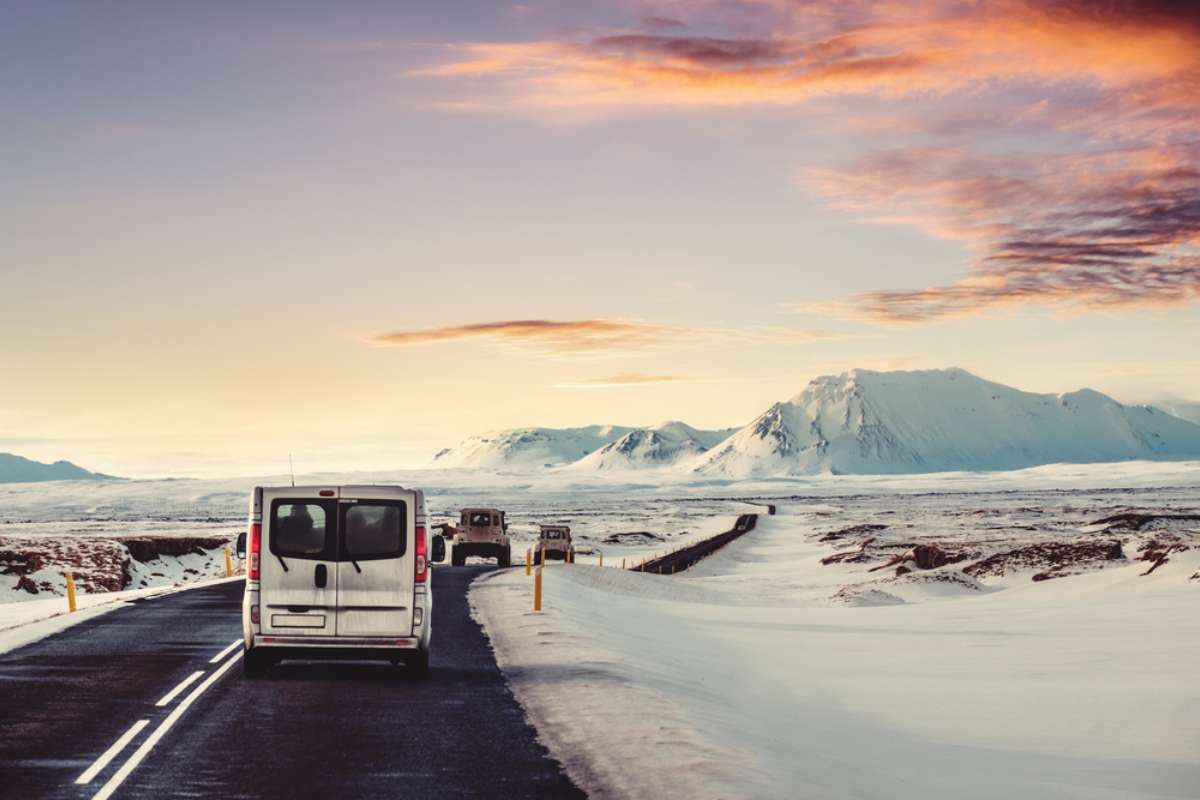White van and 4x4s on a plowed winter road at sunset in Iceland, with snow-covered plains, yellow markers.