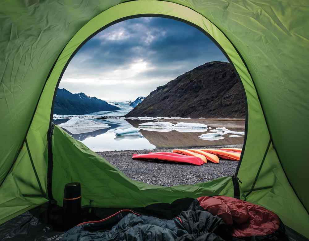 Tent view of Jökulsárlón Glacier Lagoon with icebergs, mountains, and kayaks outside.