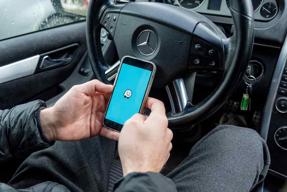 Driver holding a smartphone with the Waze app open inside a car.