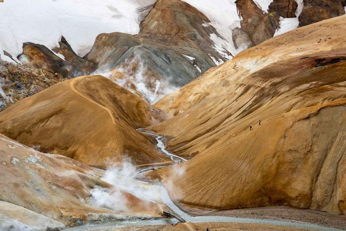 Steaming rhyolite hills and snowfields in Kerlingarfjöll, with hikers on the F35 trail.